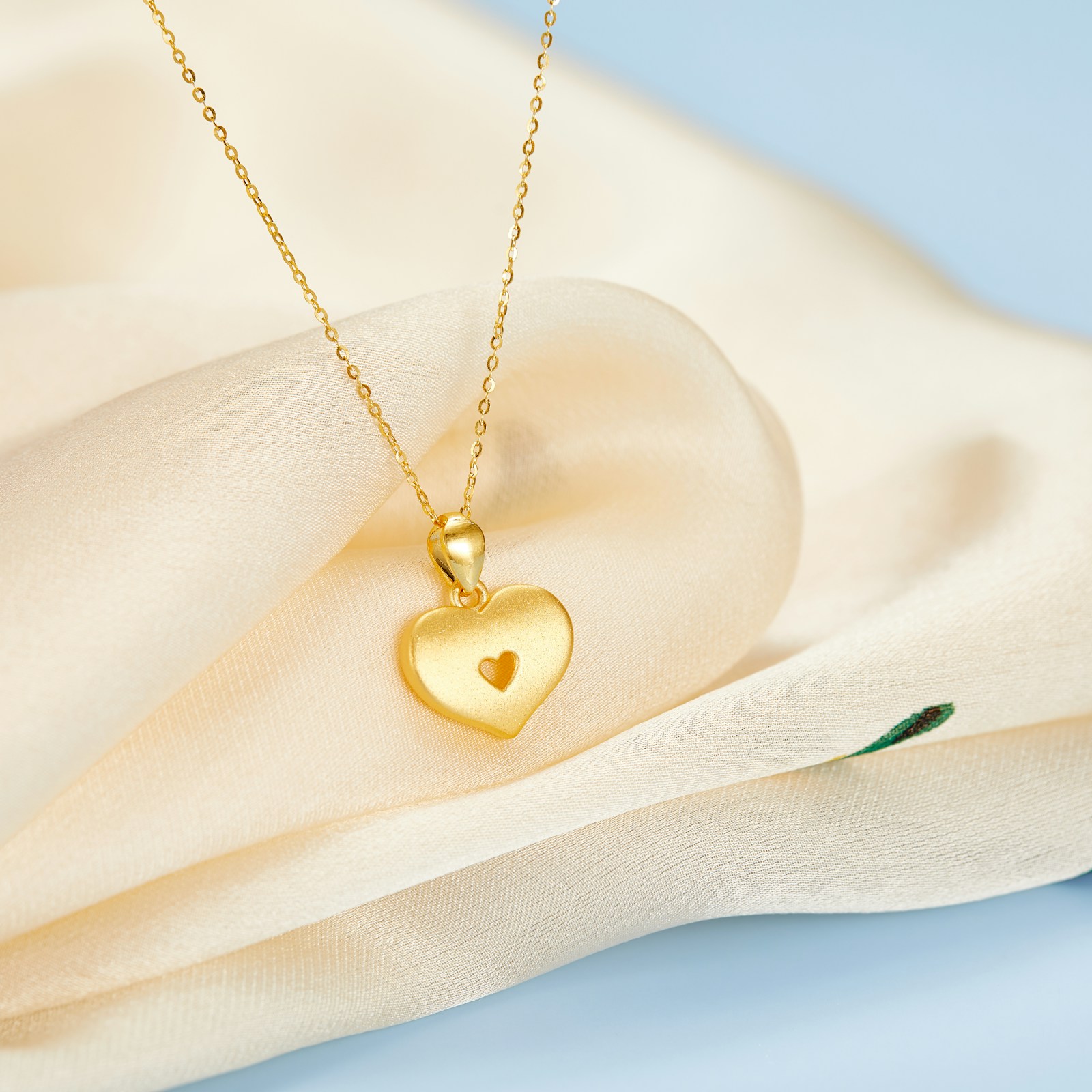 Pendentif coeur en or posé sur un tissu blanc, bijou original pour la fête des mères