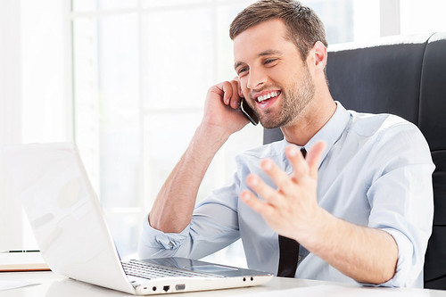 Homme en chemise bleu clair et cravate au téléphone devant son ordinateur portable