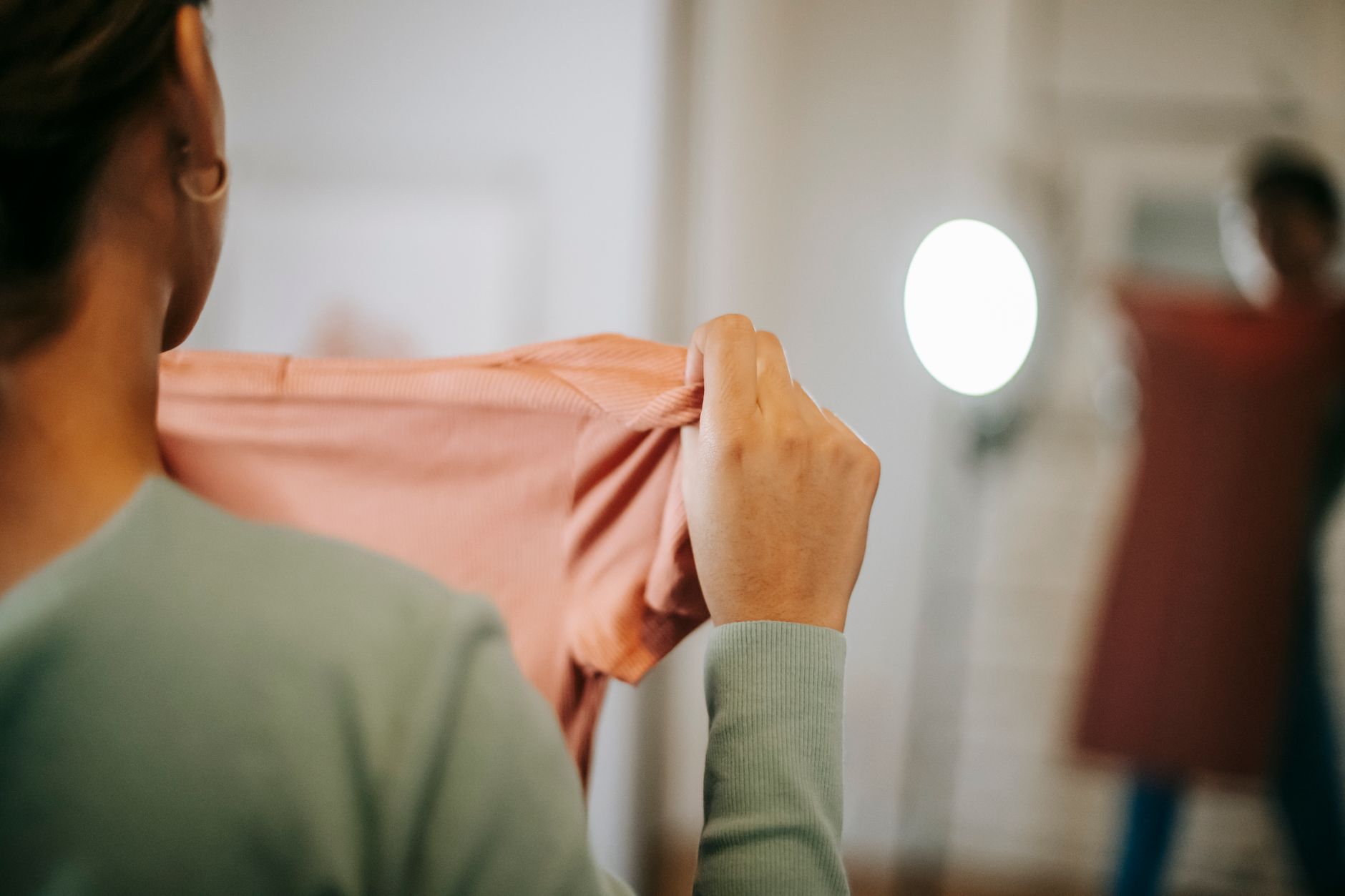 Personne tenant un vêtement rose face à un miroir pour vérifier la coupe et la taille