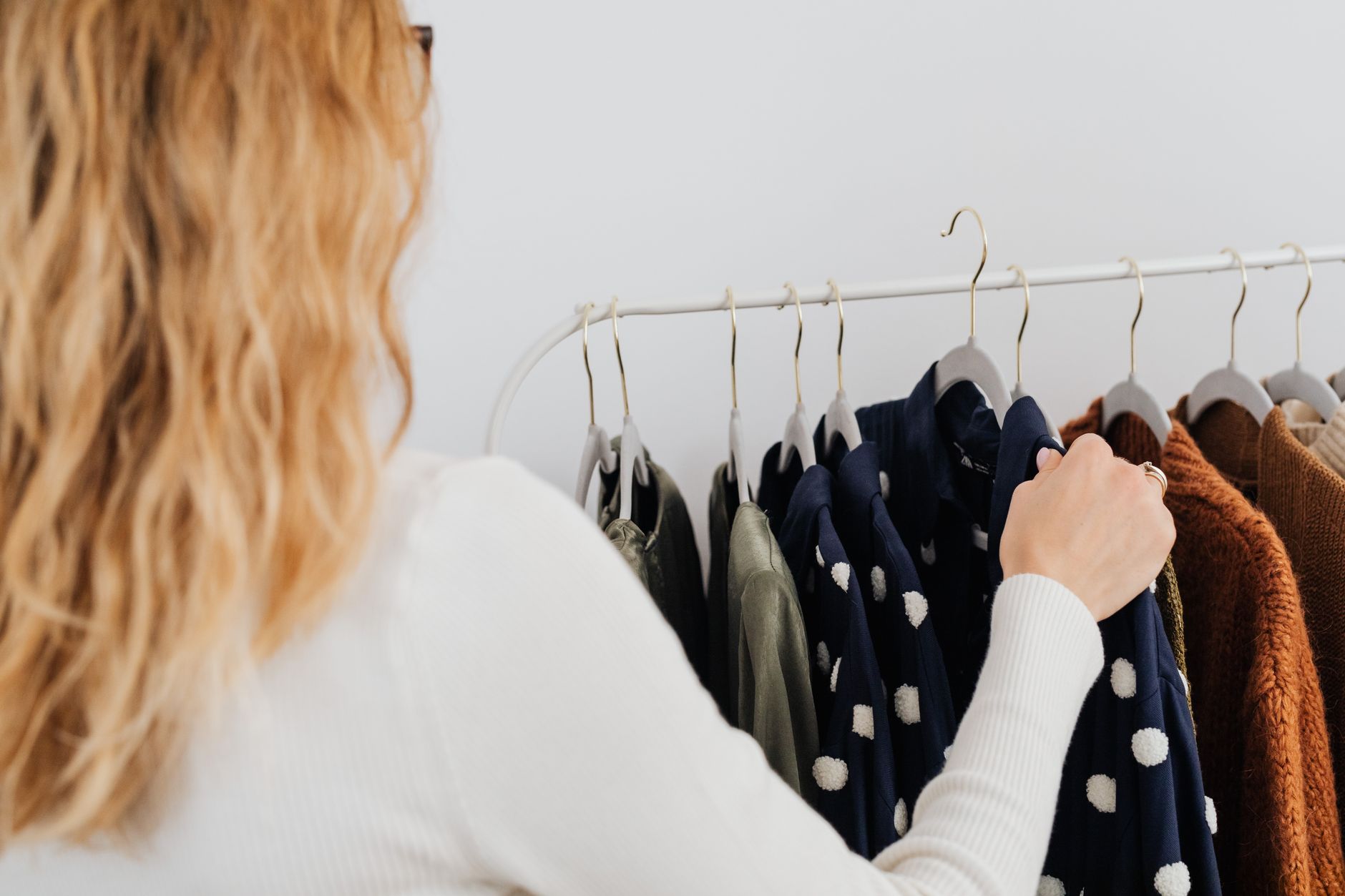 Femme choisissant un vêtement parmi des pulls et vestes aux couleurs d'automne sur un portant