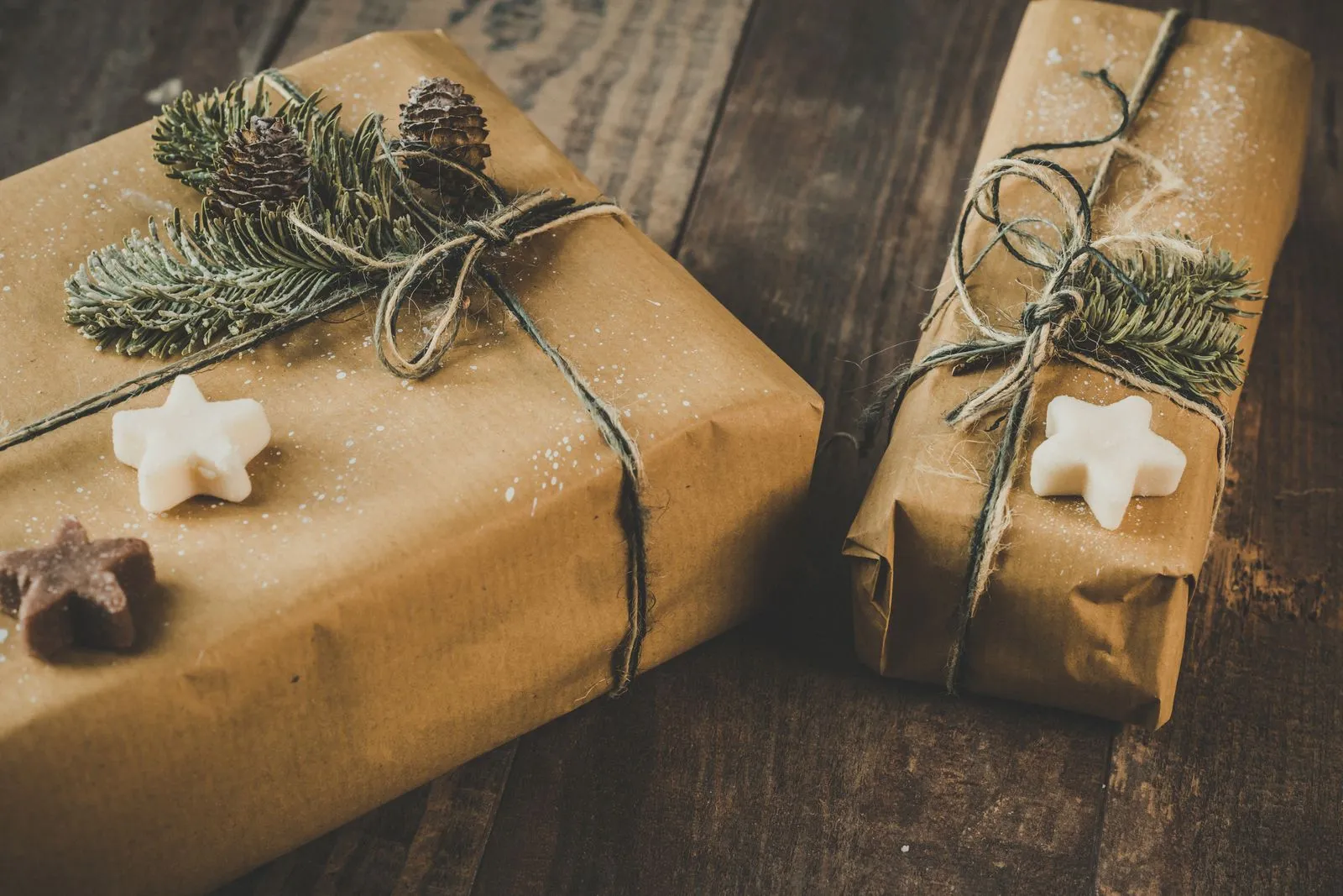 Deux paquets cadeaux en papier kraft noués de ficelle et de branches de sapin, sur une table en bois