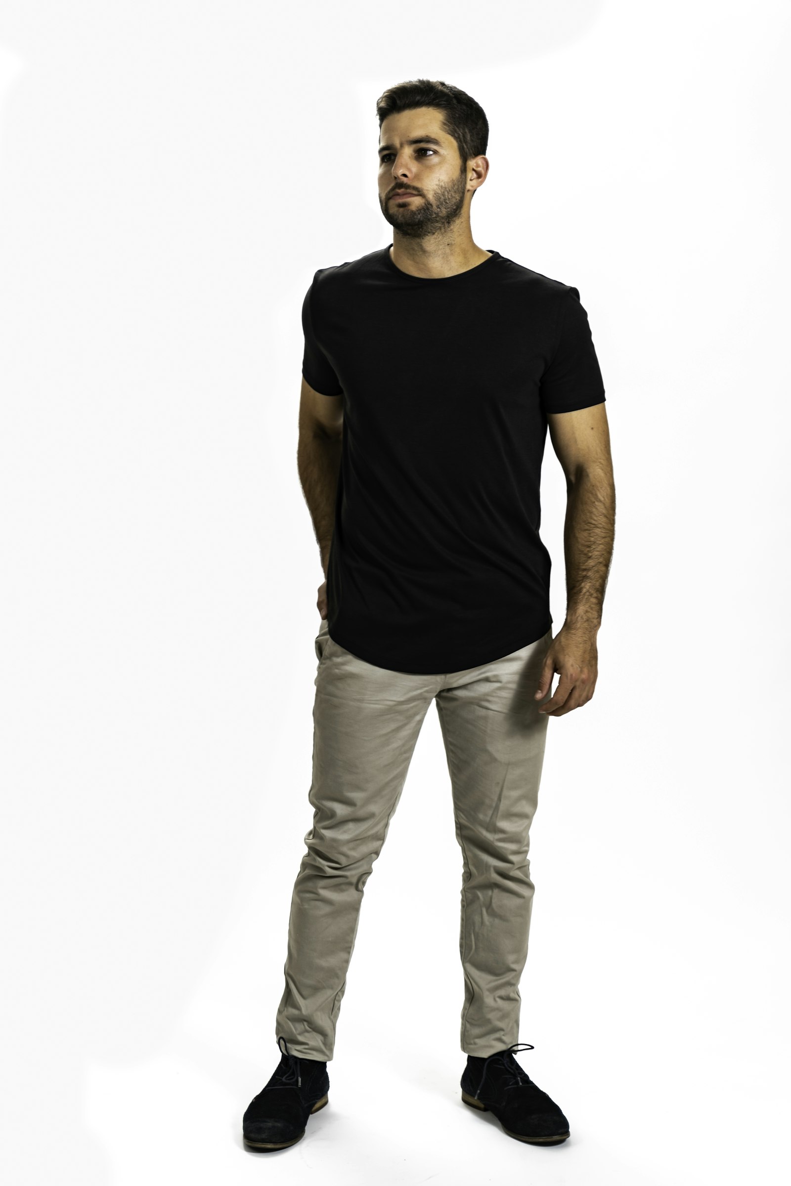 Homme portant un pantalon chino beige et un t-shirt noir sur fond blanc