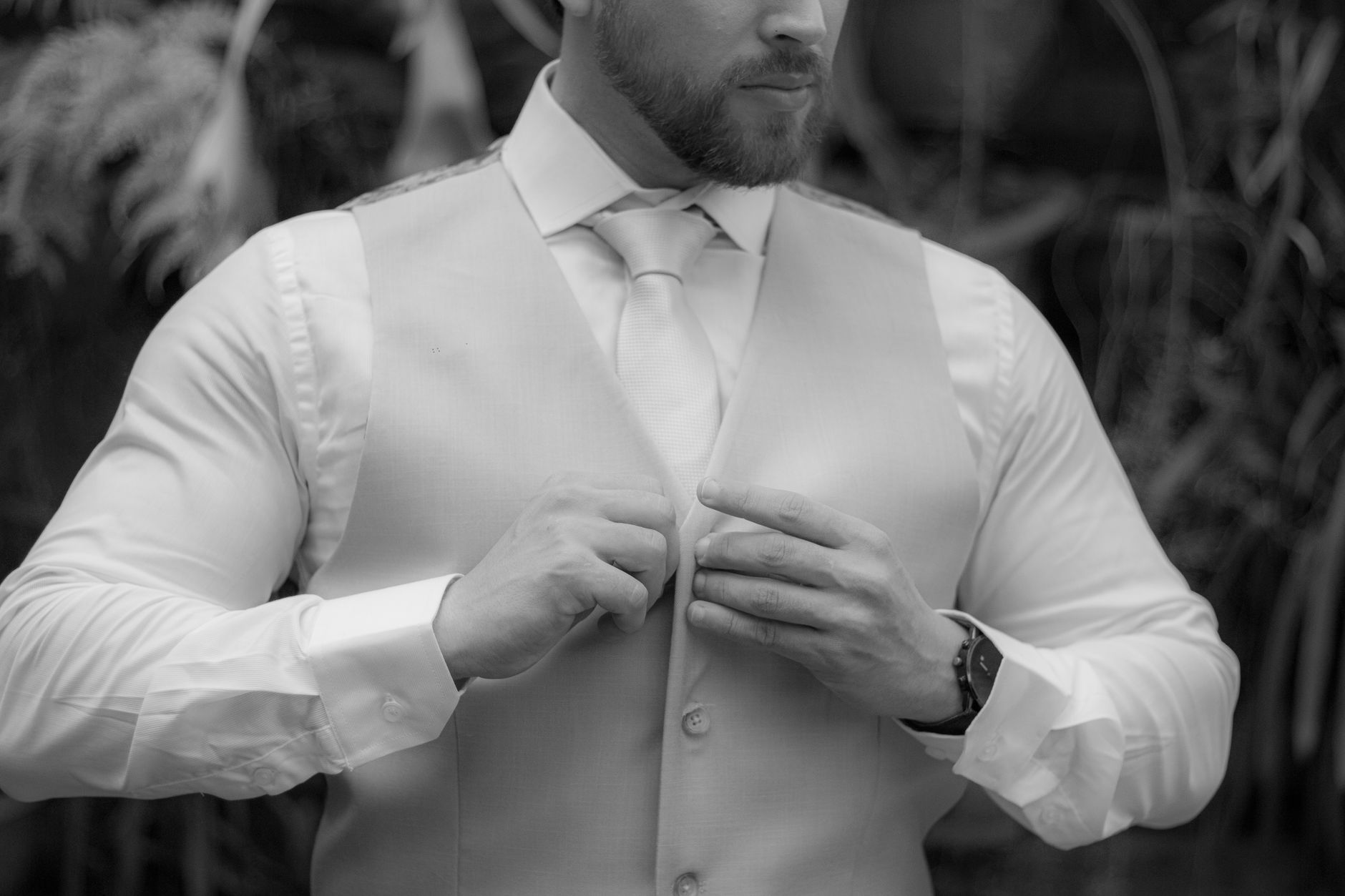 Homme ajustant son gilet sur une chemise blanche, gros plan sur le col et les manchettes boutonnées.