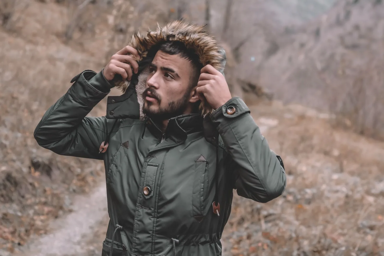 Homme ajustant la capuche d'une parka kaki dans un paysage d'hiver