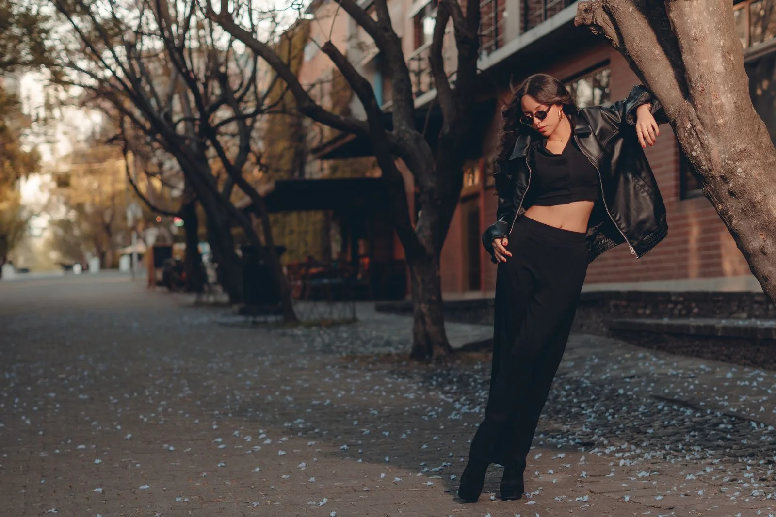 Femme en veste de cuir noire dans une rue arboree en ville
