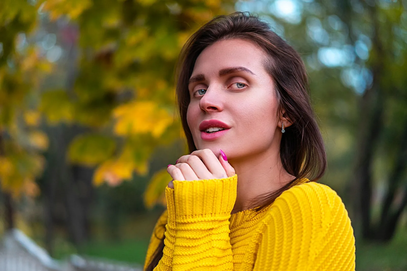 Femme en pull jaune en grosse maille côtelée devant un feuillage d'automne